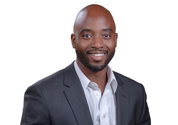 Professional headshot of Jimi Ige, MPA, CISSP, CISM, PMP, Executive Director of Nest and Rise, and Cybersecurity & AI Governance Strategist, wearing a dark gray suit jacket and white collared shirt, smiling against a white background.